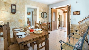 A dining area with a stone wall, wooden furniture, and a clock. - Ca'l Gall - Two Bedroom Villa, Sleeps 4 (Crestatx)