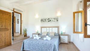 A bedroom with a bed, bedside tables, a wall-mounted light fixture, and a wooden door. - Ca'l Gall - Two Bedroom Villa, Sleeps 4 (Crestatx)