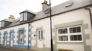 A row of townhouses with a distinct geometric pattern on the facade, a white door, and a bench outside. - Eider Cottage (Buckie)