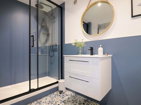 Une salle de bain dotée d’une douche à parois de verre, d’un meuble-lavabo blanc avec un miroir et de carreaux de sol à motifs.