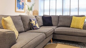 A sectional sofa with multiple cushions, a patterned rug, and a framed artwork on the wall. - Eider Cottage (Buckie)