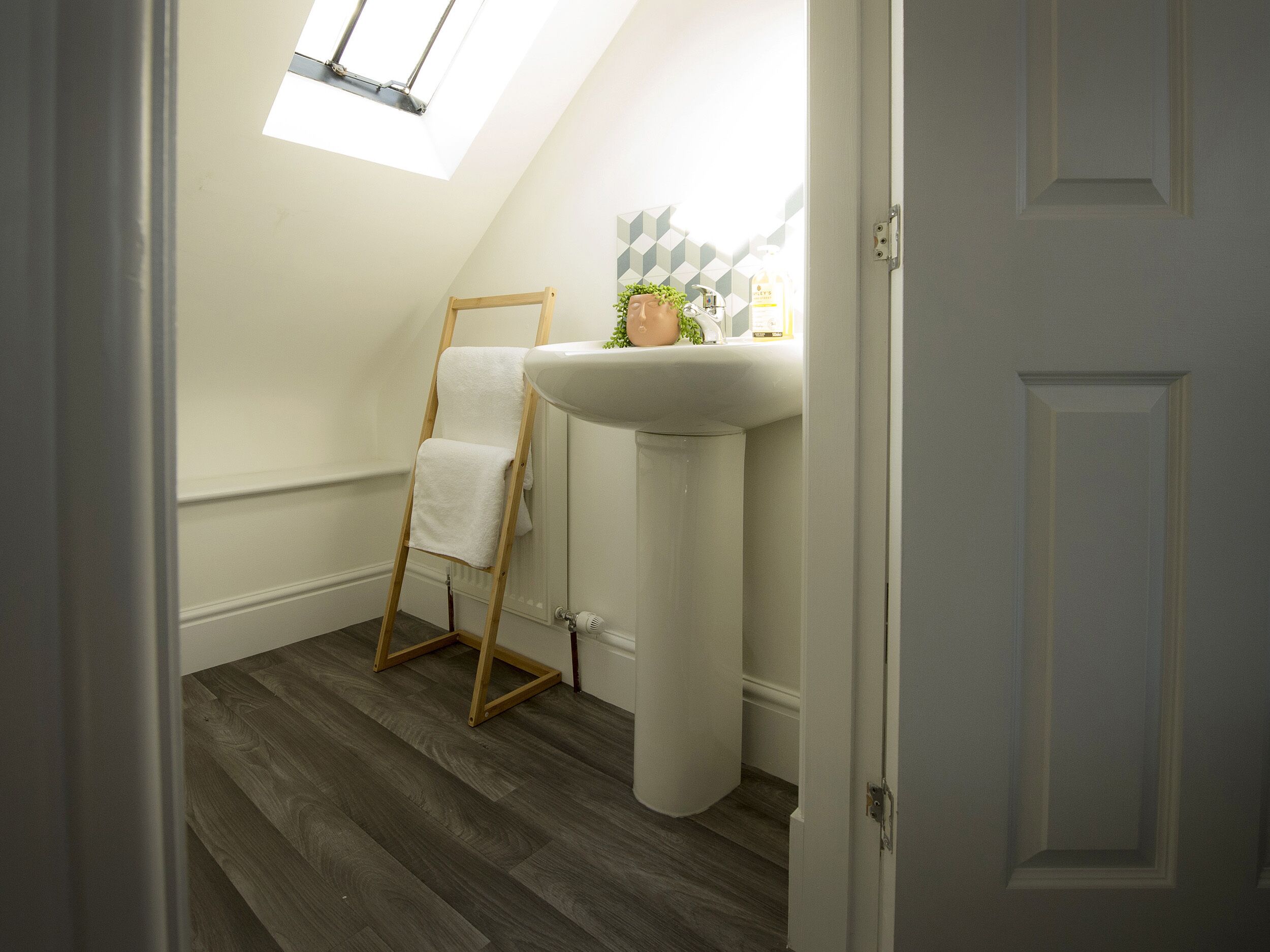 A bathroom with a wooden ladder, a white sink, and a window above the sink.