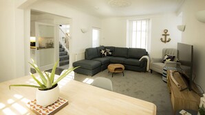 Una sala moderna con un sofá seccional, una mesa de comedor con una planta y un mueble para televisión.