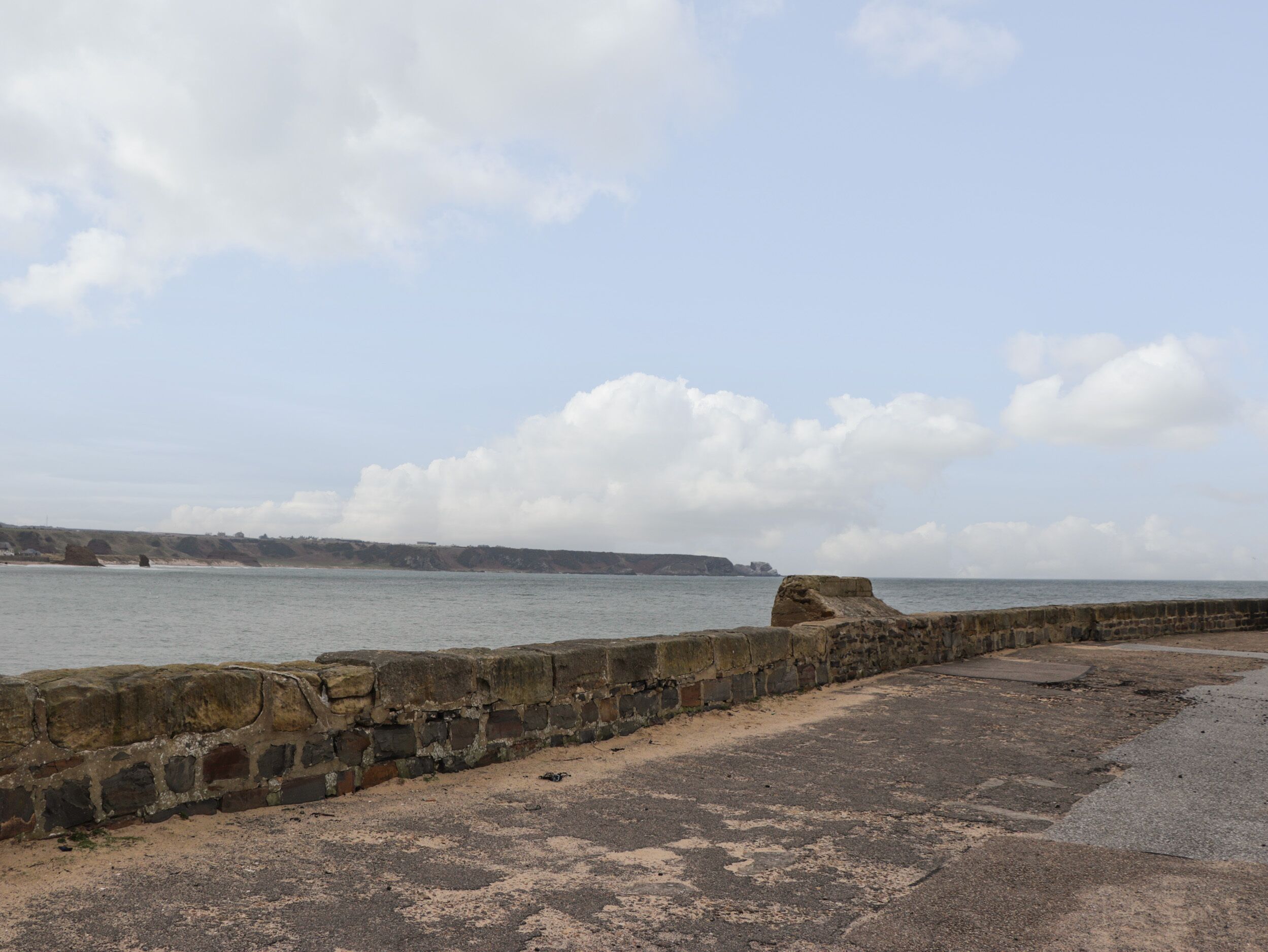 A coastal view with a stone wall and sandy beach.