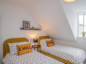 A bedroom with two beds, each with polka dot bedding and pillows with the word "CHILL". There is a shelf with a framed picture and a small plant. - Sandpiper Cottage (Buckie)