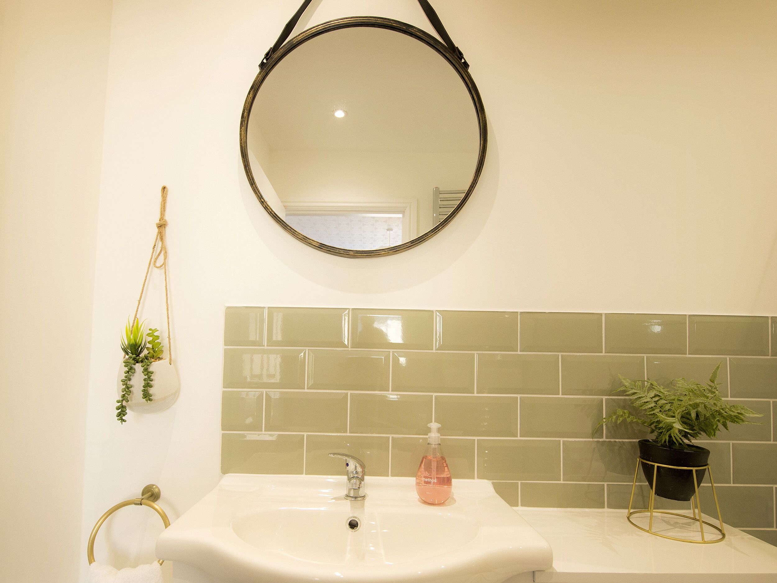 A bathroom with a round mirror, a sink, a towel rack, and a potted plant.