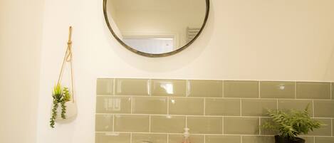 A bathroom with a round mirror, a sink, a towel rack, and a potted plant.