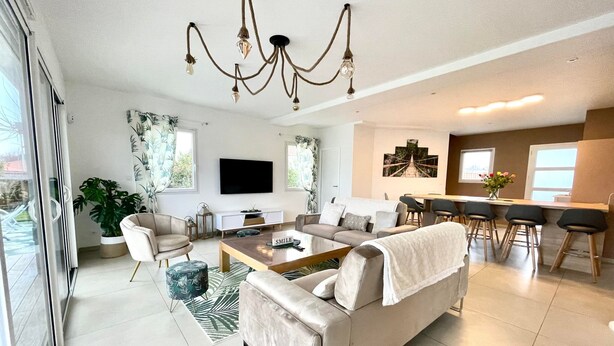Ein modernes Wohnzimmer mit einer Couch, einem Couchtisch und einem Fernseher. Es gibt einen Essbereich mit Stühlen und einem Tisch.