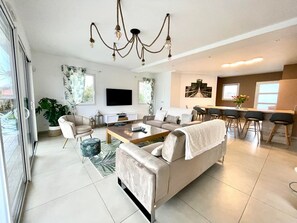 Een moderne woonkamer met een bank, salontafel en televisie. Er is een eethoek met stoelen en een tafel.