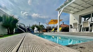 Ein Schwimmbecken mit Holzterrasse, Liegestühlen und einem gelben Sonnenschirm.