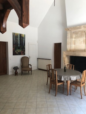Uma sala de jantar com uma mesa redonda, cadeiras, lareira e um quadro na parede.