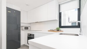 Una cocina moderna con armarios blancos, microondas integrado, una pequeña isla con fregadero y una ventana que proporciona luz natural.