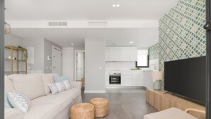 Una sala de estar moderna con un sofá, otomanas y un televisor. Cuenta con una cocina con armarios y una encimera.