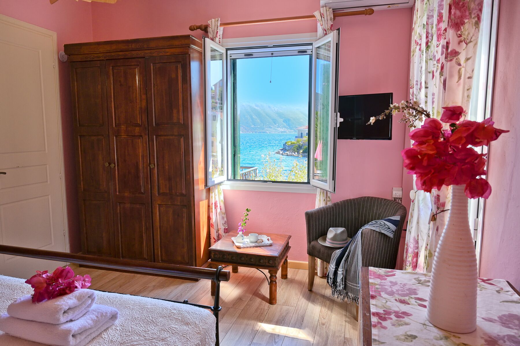 Une pièce avec une armoire en bois, une petite table sur laquelle se trouve une théière, une chaise et une vue sur la mer par la fenêtre.