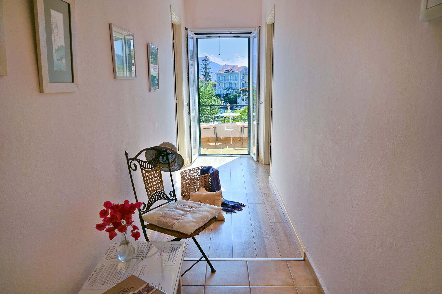 Un couloir avec une chaise, une petite table ornée d’un vase de fleurs et une vue sur un balcon aménagé avec du mobilier d’extérieur.