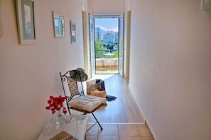 A hallway with a chair, a small table with a vase of flowers, and a view of a balcony with outdoor furniture.