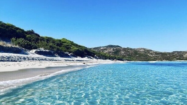 Una spiaggia ampia e poco profonda, con sabbia bianca e acque turchesi calme.