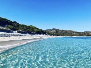 A clear, shallow beach with white sand and calm turquoise waters.
