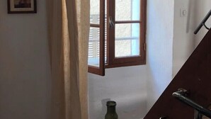 Una stanza con una finestra con cornice in legno, una tenda e una bottiglia verde sul pavimento.