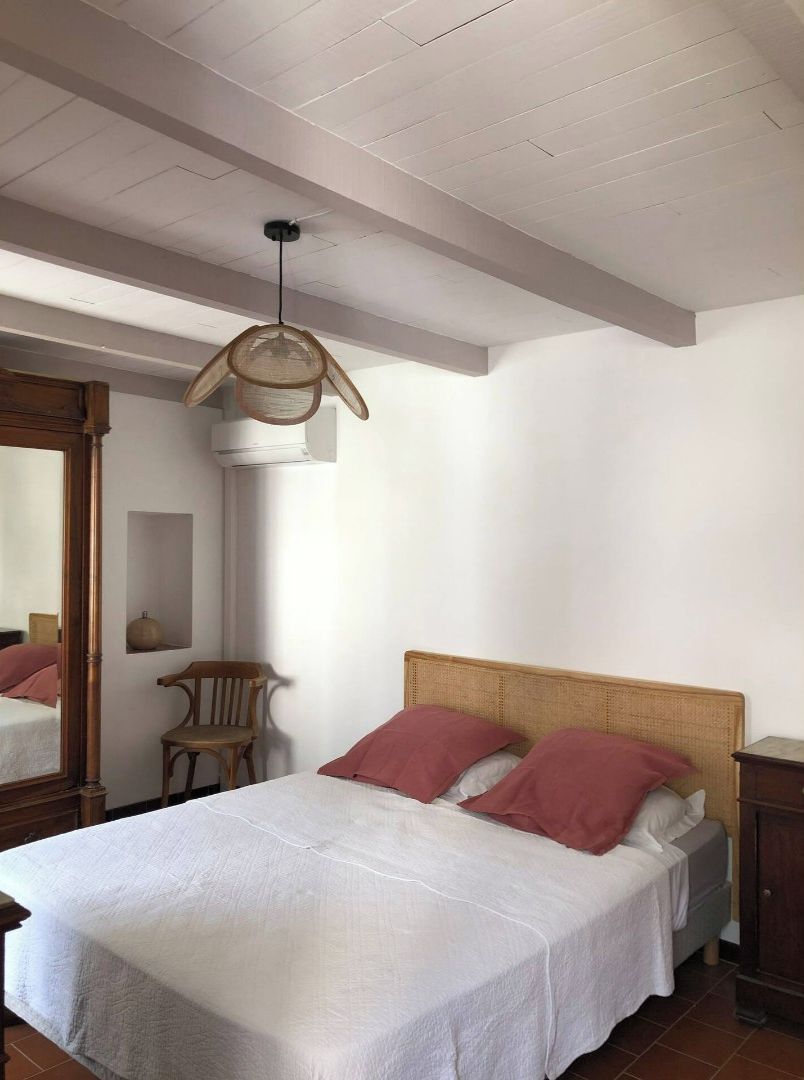 Une chambre à coucher avec un lit, une chaise en bois, un luminaire suspendu et un miroir.