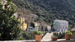 Una terrazza con sedie e tavolo di legno, affacciata su un paesaggio montuoso con edifici e vegetazione.