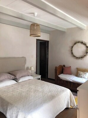 A bedroom with two beds, a hanging light fixture, a door, and a wall wreath.