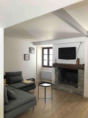 A living room with a fireplace, a sofa, a small round table, and a TV mounted on the wall.