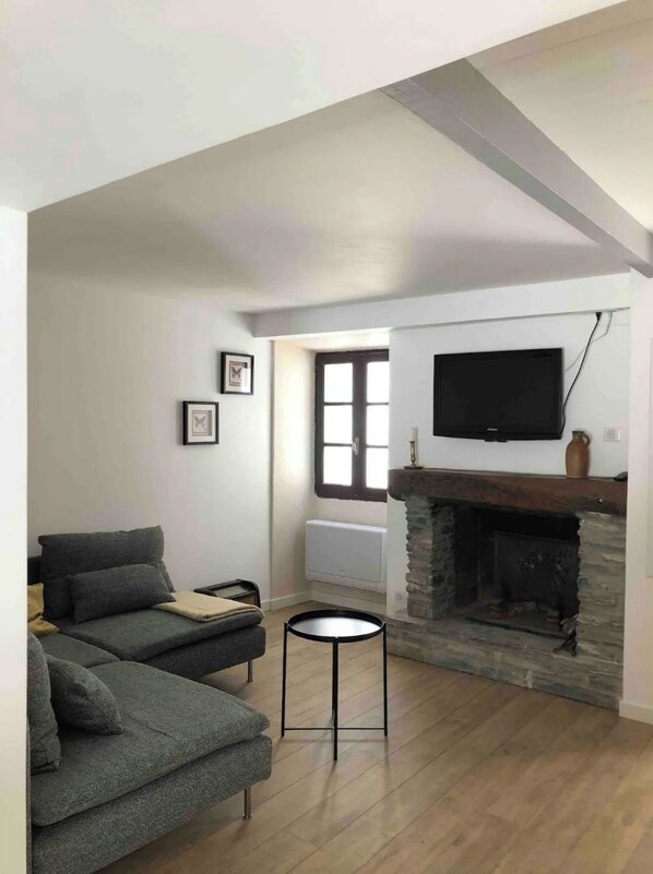 A living room with a grey sofa, a fireplace, a television mounted above it, and a small round table.