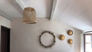 Una stanza accogliente con una panca in legno, una lampada in fibra naturale, una ghirlanda decorativa e un cappello appeso al muro.