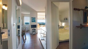 Quarto de hotel com cama, televisão, escrivaninha e cadeira. Há uma janela com vista para o exterior.