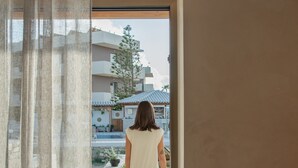 Valkoiseen mekkoon pukeutunut henkilö kävelee ovesta sisäpihalle, jossa on uima-allas ja ruukkukasveja.
