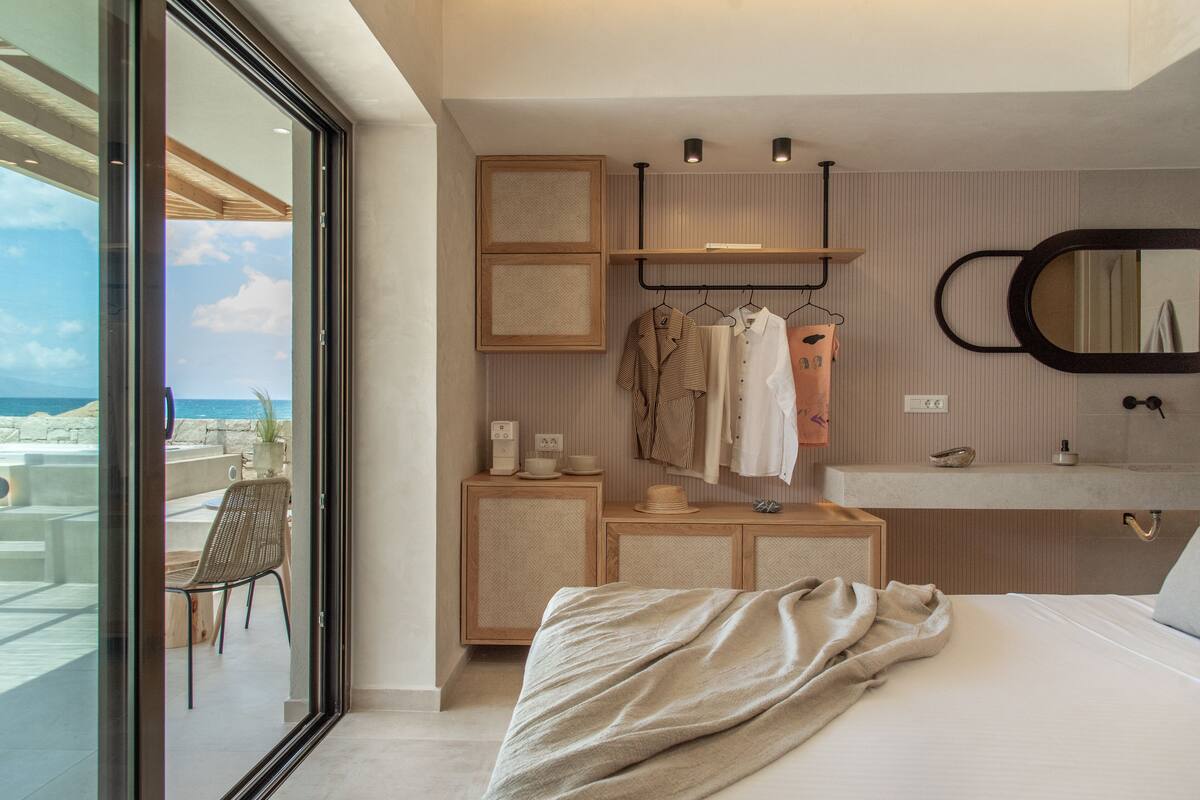 A modern hotel room with a large bed, a bedside table, a mirror, a wardrobe, and a view of the ocean.