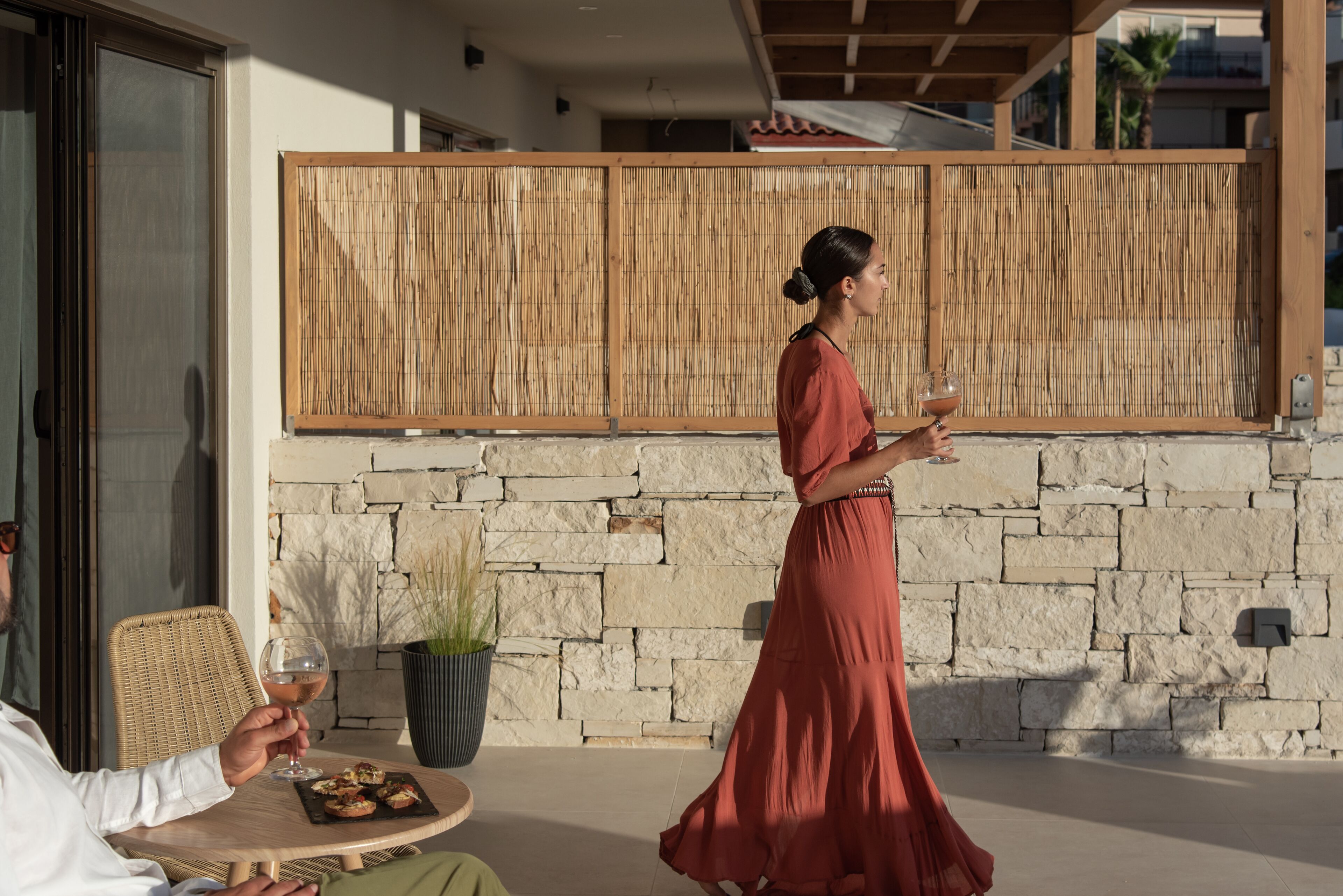 A woman in a red dress walking past a table with a glass of wine and a plate of food.