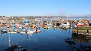 A harbor with numerous boats docked, a crane, and a distant view of a town. - Chydour (Penzance)