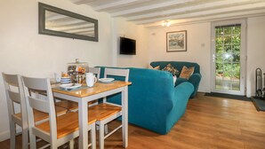 A cozy living area with a wooden dining table, white chairs, a teal sofa, and a television mounted on the wall. - Chydour (Penzance)