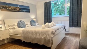 A modern bedroom with a bed, bedside tables, a window with curtains, and a view of greenery outside. - Chydour (Penzance)