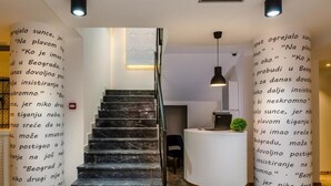 Eine Hotelhalle mit einer Marmortreppe, einer Rezeption und dekorativen Säulen mit Schrift.