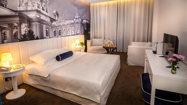 Ein Hotelzimmer mit einem großen Bett, einem Schreibtisch, einem Sessel, einem kleinen Tisch und einem Wandbild.
