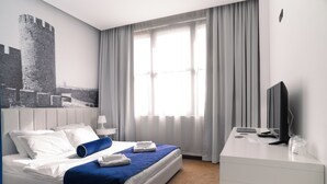 Ein Hotelzimmer mit Bett, Schreibtisch, Fernseher und einem großen Fenster mit Vorhängen.