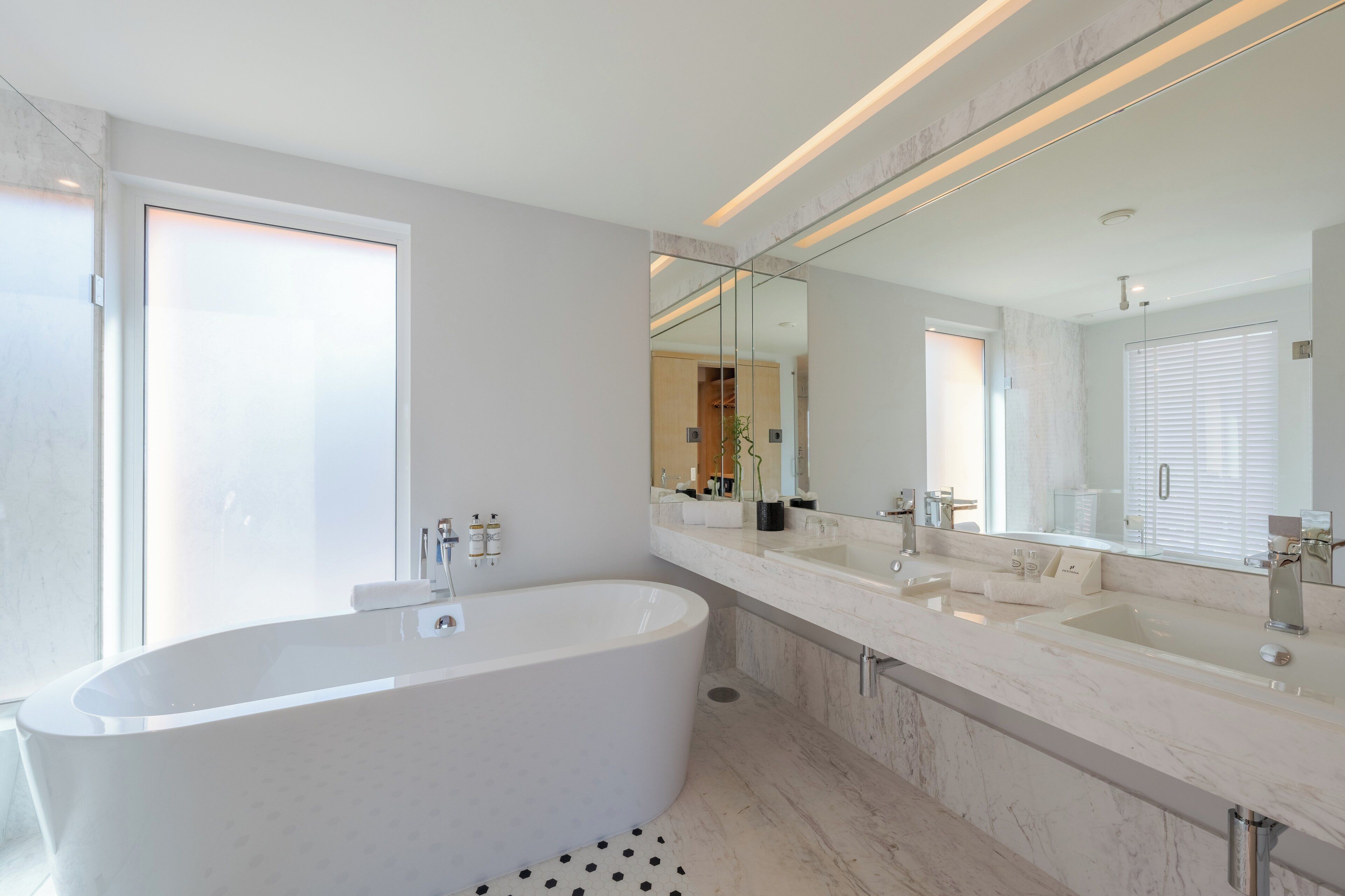 A modern bathroom with a freestanding bathtub, a large mirror, and a double sink vanity.