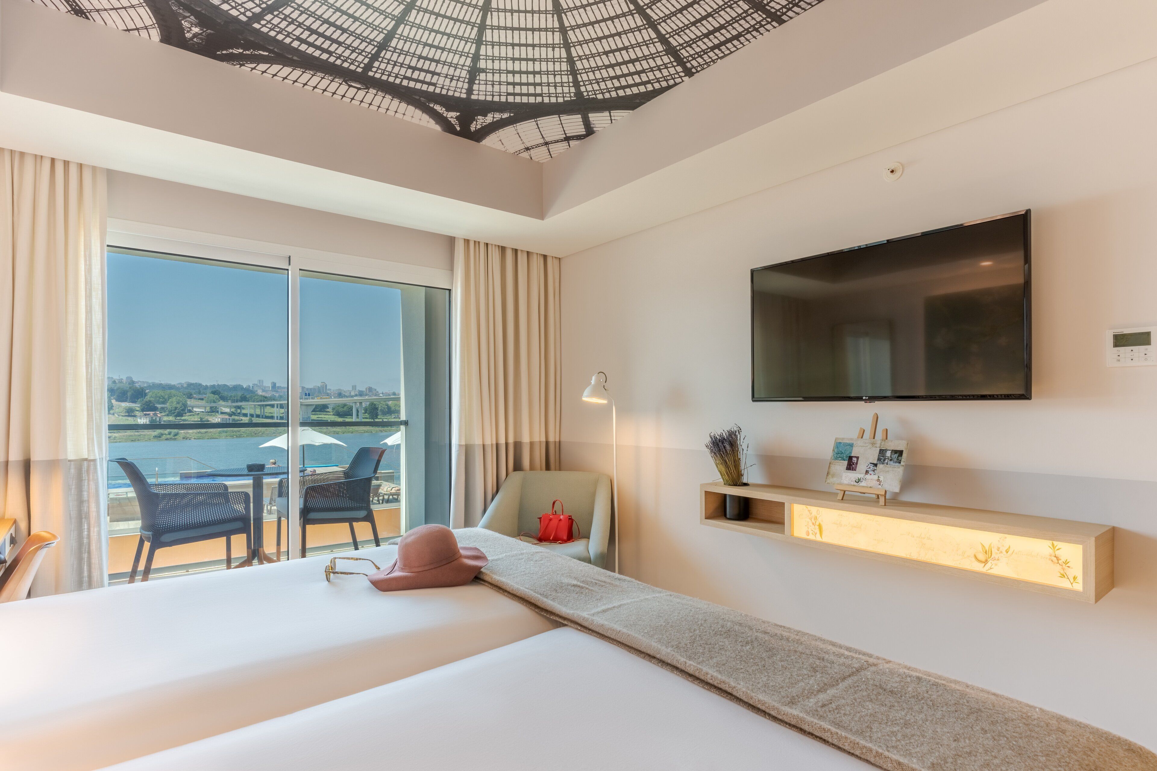 Ein modernes Hotelzimmer mit einem großen Bett, einem an der Wand befestigten Fernseher, einem Balkon mit Stadtblick und einem Schreibtisch mit Stuhl.