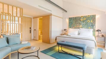 A modern hotel room with a bed, a sofa, a bench, a small table, and a wall with a floral mural.
