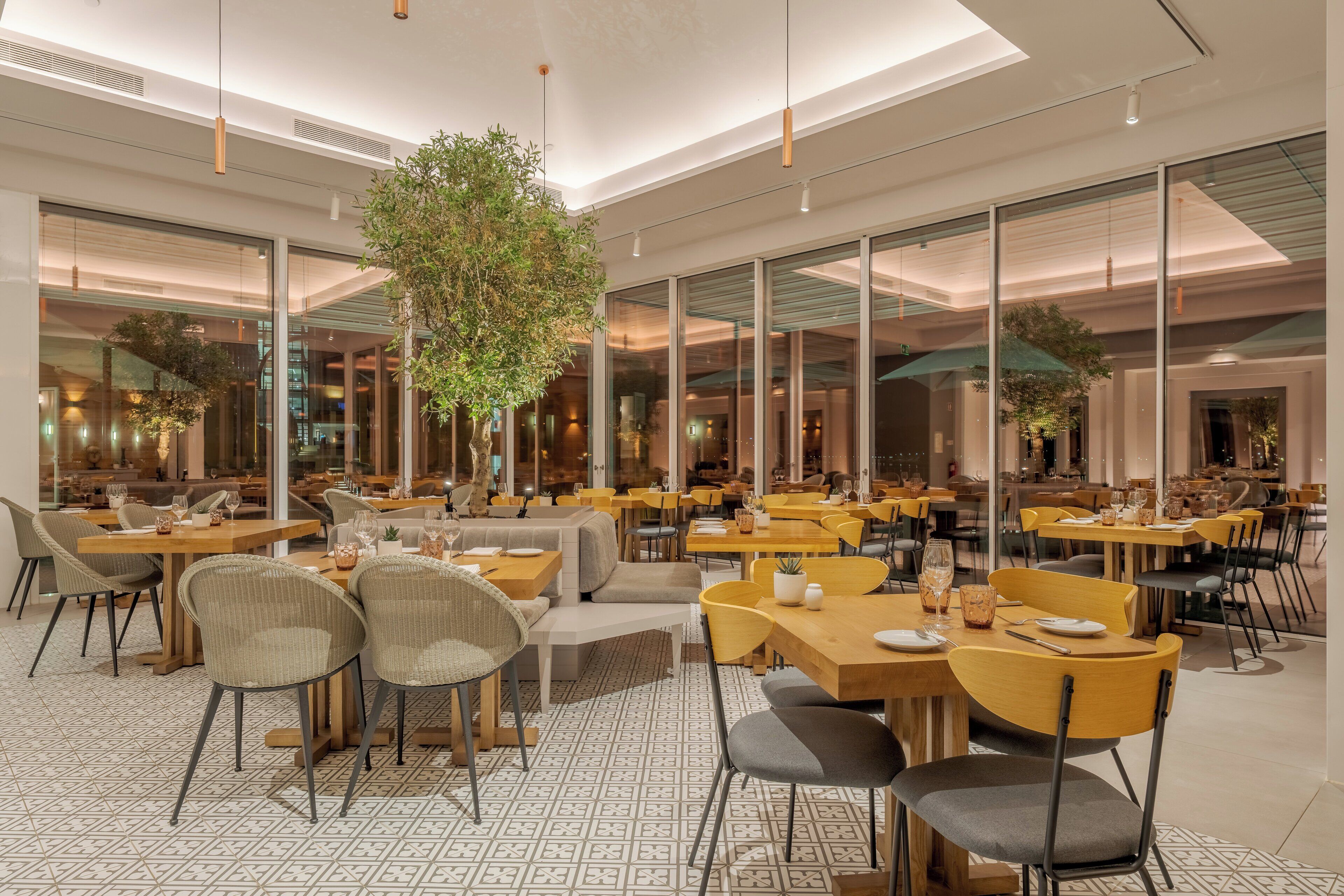 Un restaurante moderno con paredes de vidrio, varias zonas de comedor y una planta central.