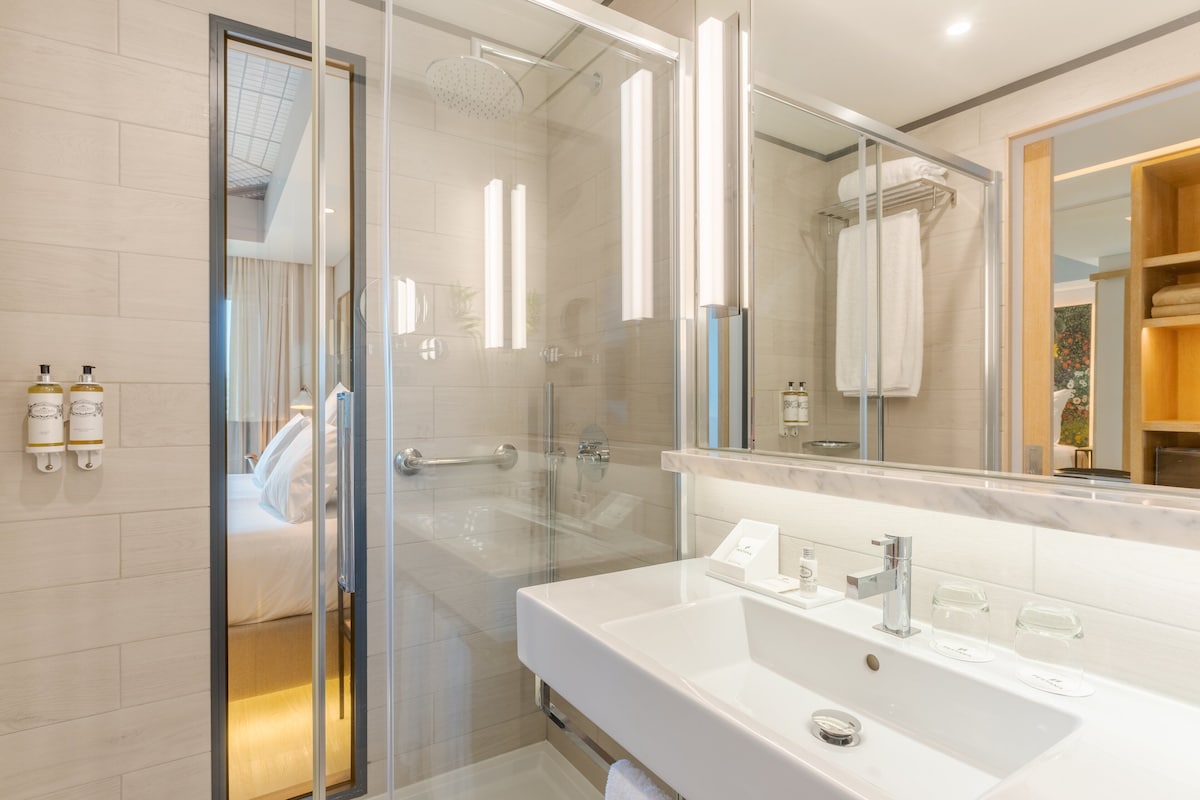 A modern bathroom with a glass-enclosed shower, a large mirror, and a white sink.
