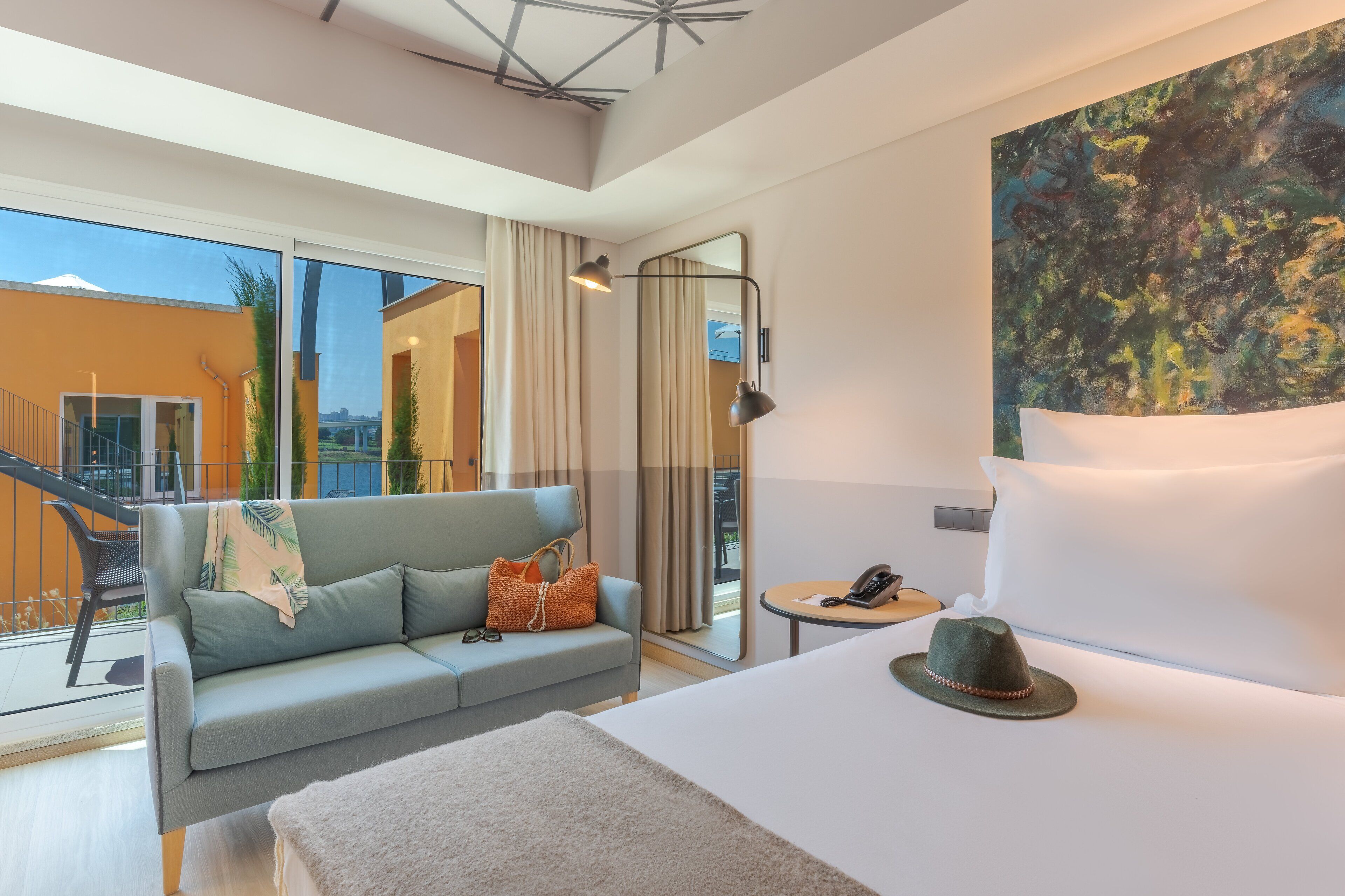 A hotel room with a large bed, a sofa, a small table, and a painting on the wall.
