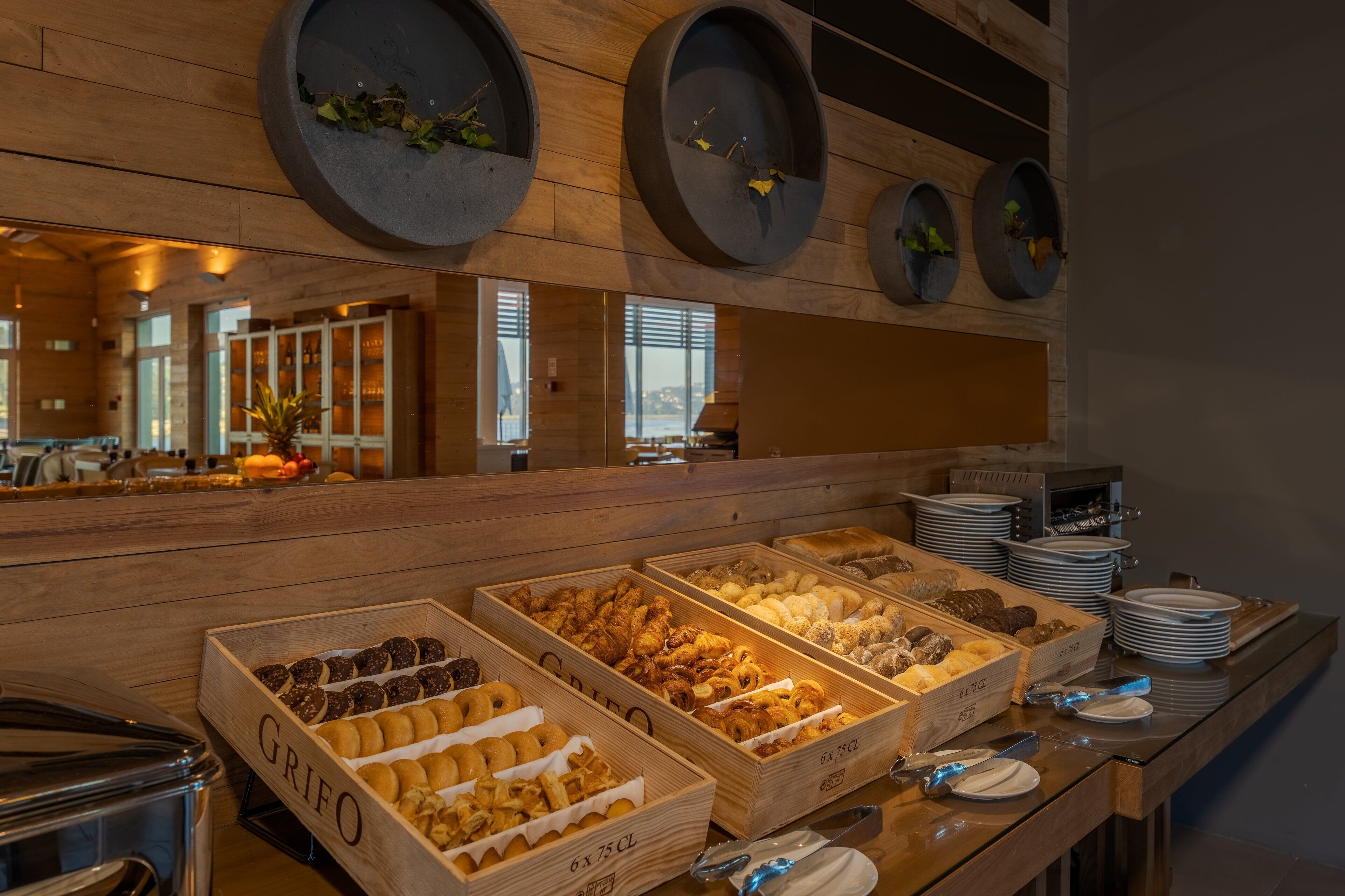 Een buffetgedeelte met diverse etenswaren in houten dozen, een toonbank met borden, en een houten wand met ronde plantenbakken.