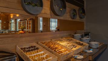 Een buffetgedeelte met diverse etenswaren in houten dozen, een toonbank met borden, en een houten wand met ronde plantenbakken.