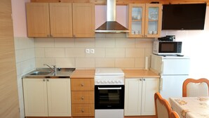 A compact kitchen with wooden cabinets, a built-in microwave, a stove, and a small dining area with a table and chairs. - Apartment Jorsi With Mountain View (Zrece)