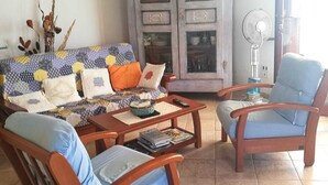 Un salon comprenant un canapé, deux fauteuils en bois, une table basse, un meuble et un ventilateur.