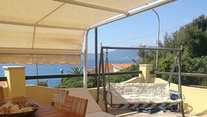 An outdoor patio with a wooden table and chairs, a swing, and a view of the sea. - Villa Marina on the waterfront I.U.N. code R9661 (Magomadas)
